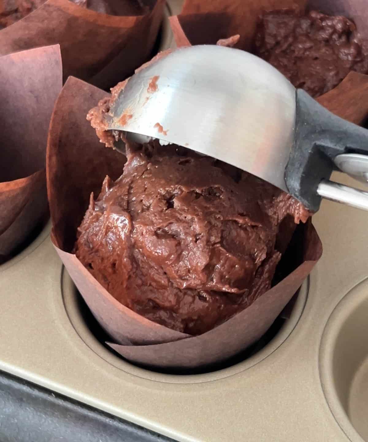 ice cream scoop dropping a scoop of chocolate muffin batter into muffin liner.