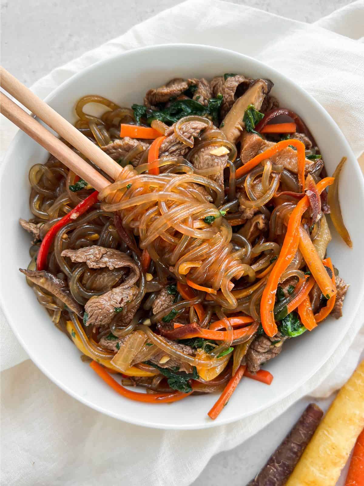 Overhead shot of beef japchae with some noodles swirled around chopsticks. 