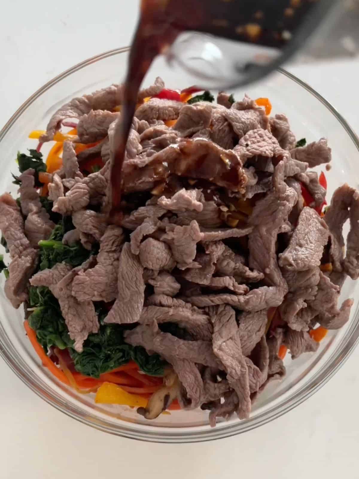 All ingredients for beef japchae in a mixing bowl with the sauce being poured on top. 