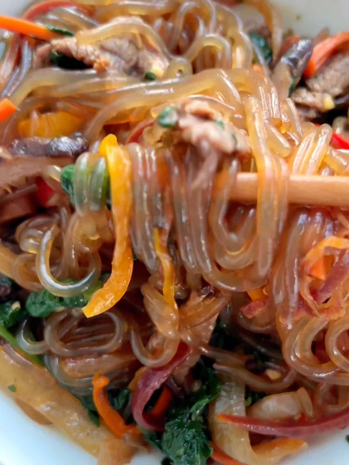 Beef japchae noodles in a bowl with chopsticks picking some up. 