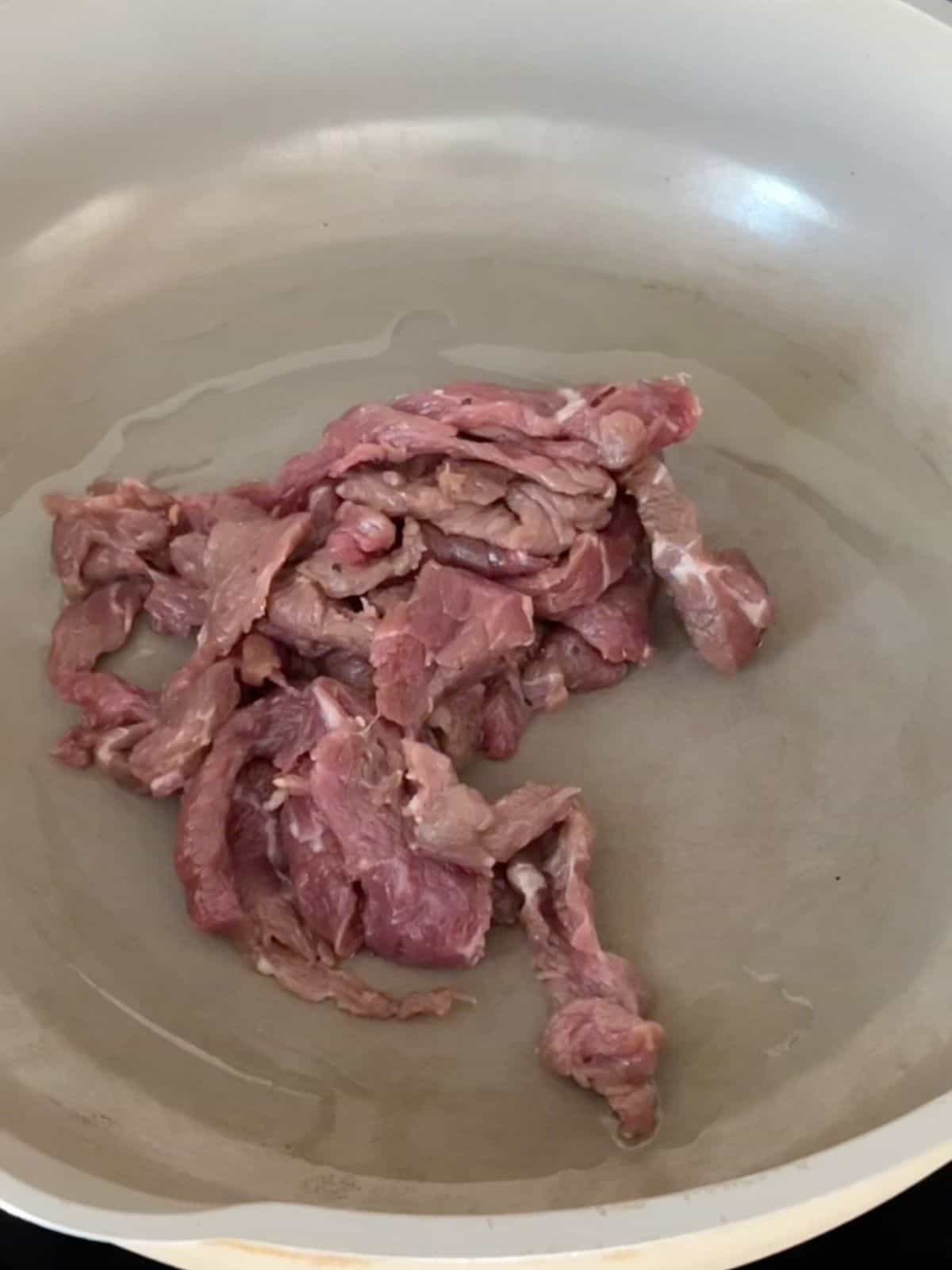 Sliced beef being seared in a skillet. 