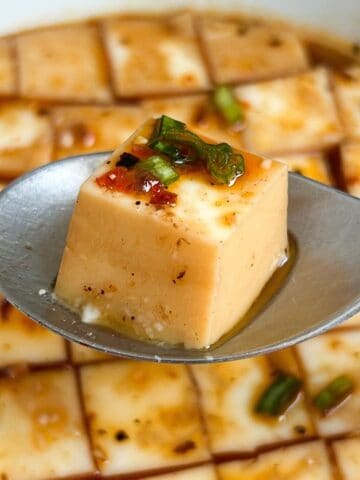 Cube of steamed egg white on a spoon with more steamed egg whites in the background.