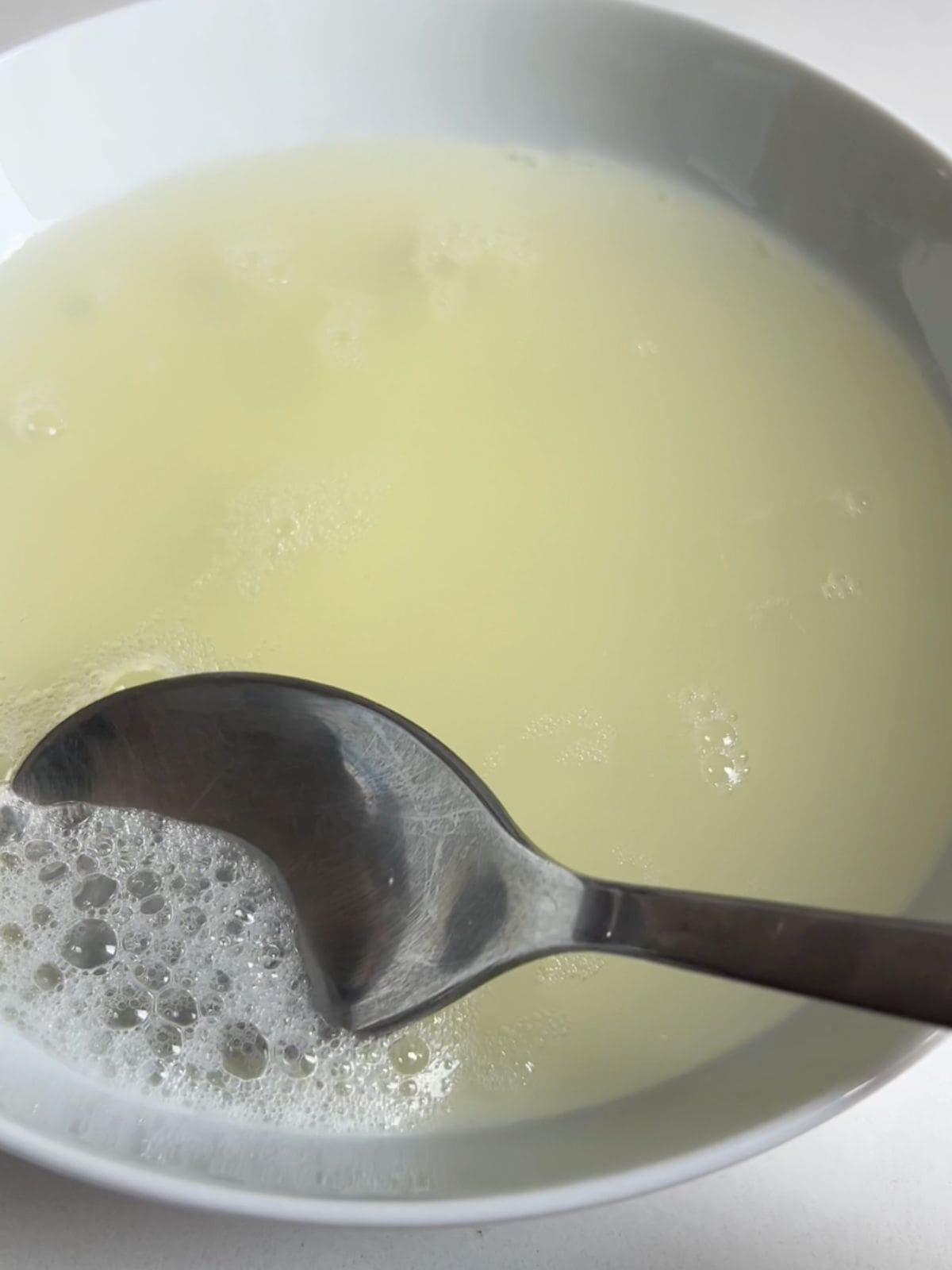 Skimming the air bubbles off of the top of the egg whites with a spoon in a bowl.