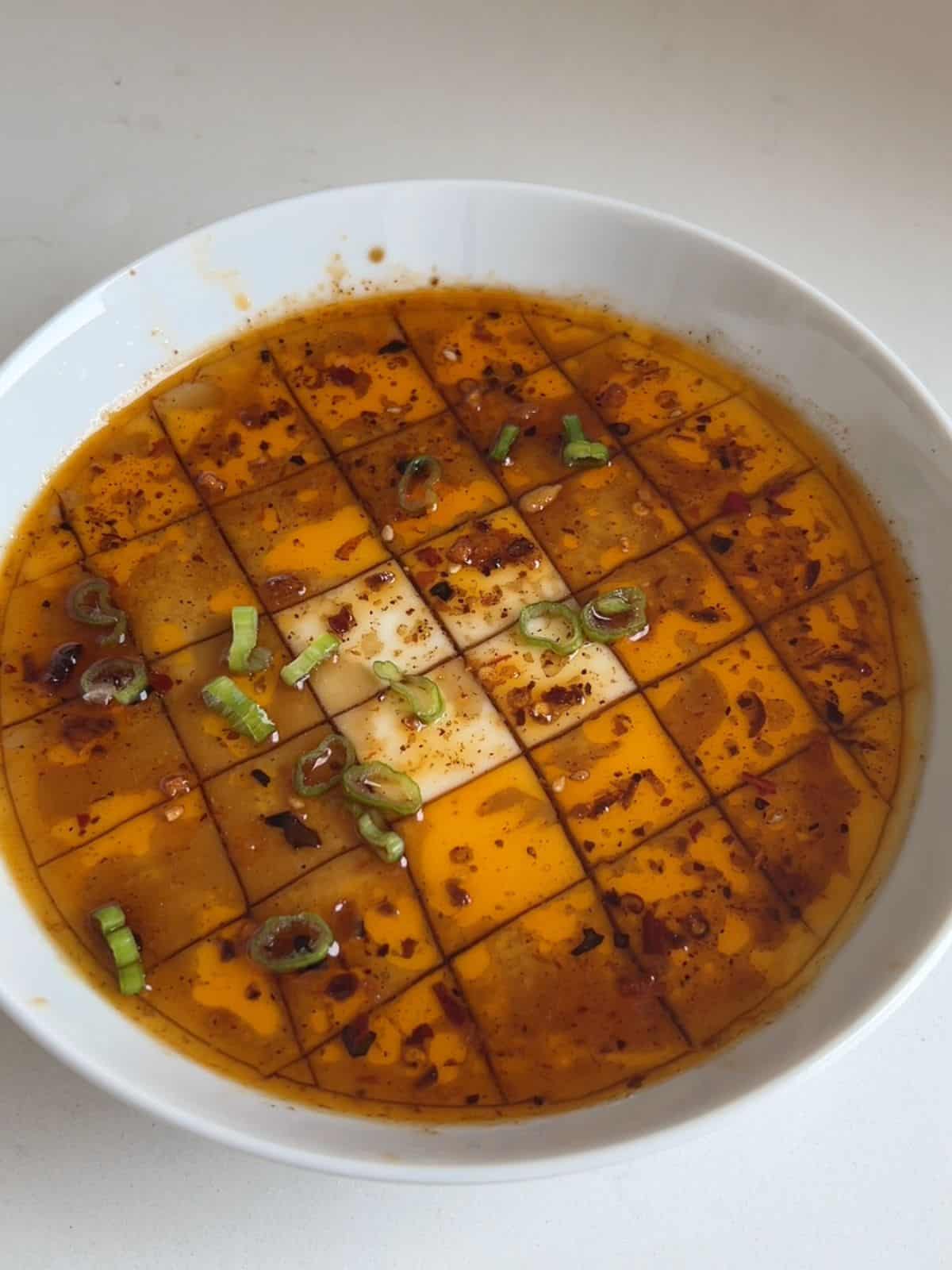 Chinese steamed egg whites in a bowl cut into cubes and topped with soy sauce, chile oil and scallions.