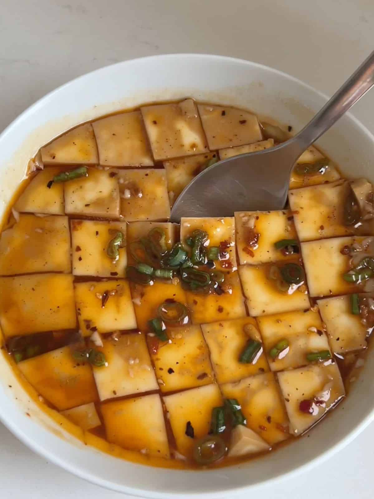 Chinese steamed egg whites in a bowl sliced into cubes with a spoon in the middle.