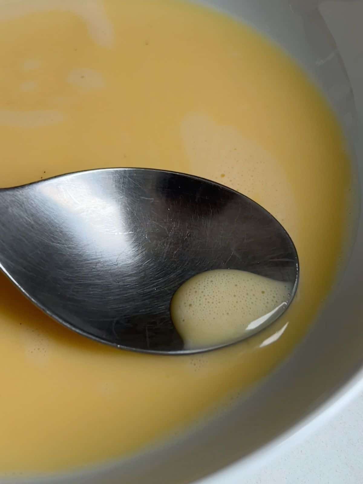 Using a spoon to remove air bubbles from the flan mixture before cooking. 