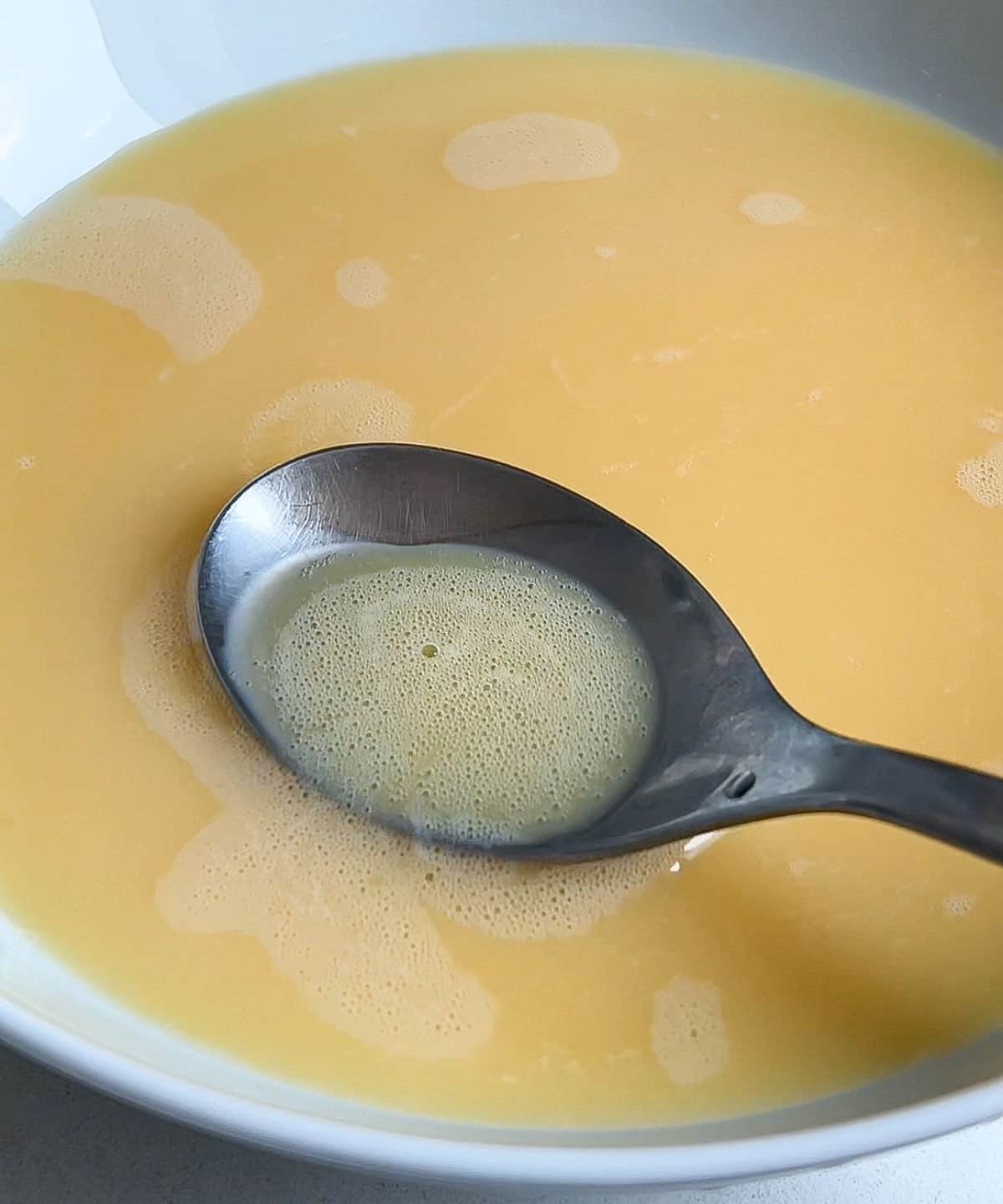 spoon scooping out the air bubbles in the egg mixture.