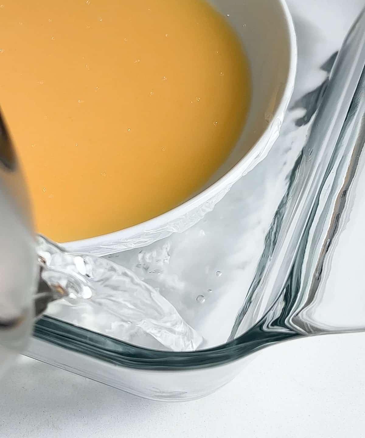 water being poured into a microwave safe dish to make the water bath for the microwaved steamed flan.