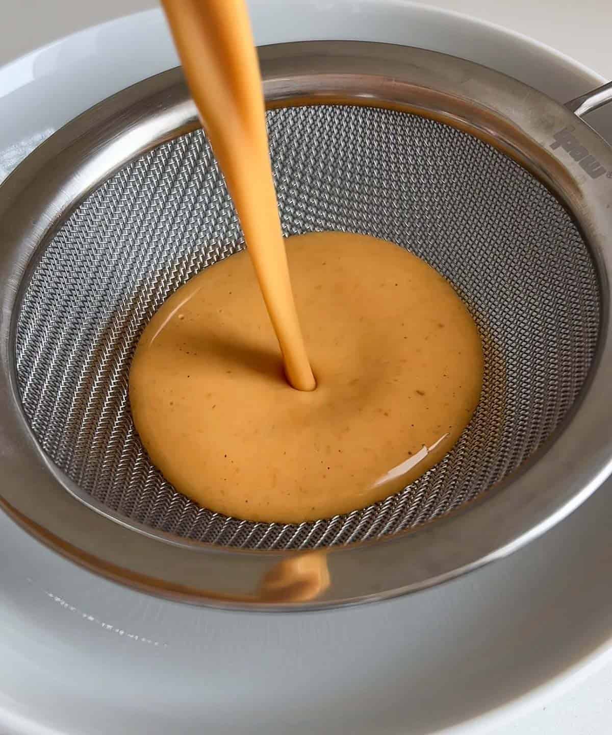 pumpkin mixture poured through a fine mesh sieve into a microwave safe bowl.