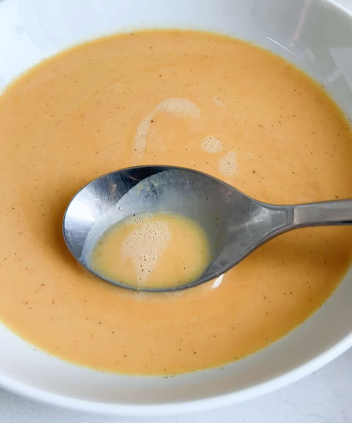 spoon scooping out the air bubbles in the pumpkin flan mixture.