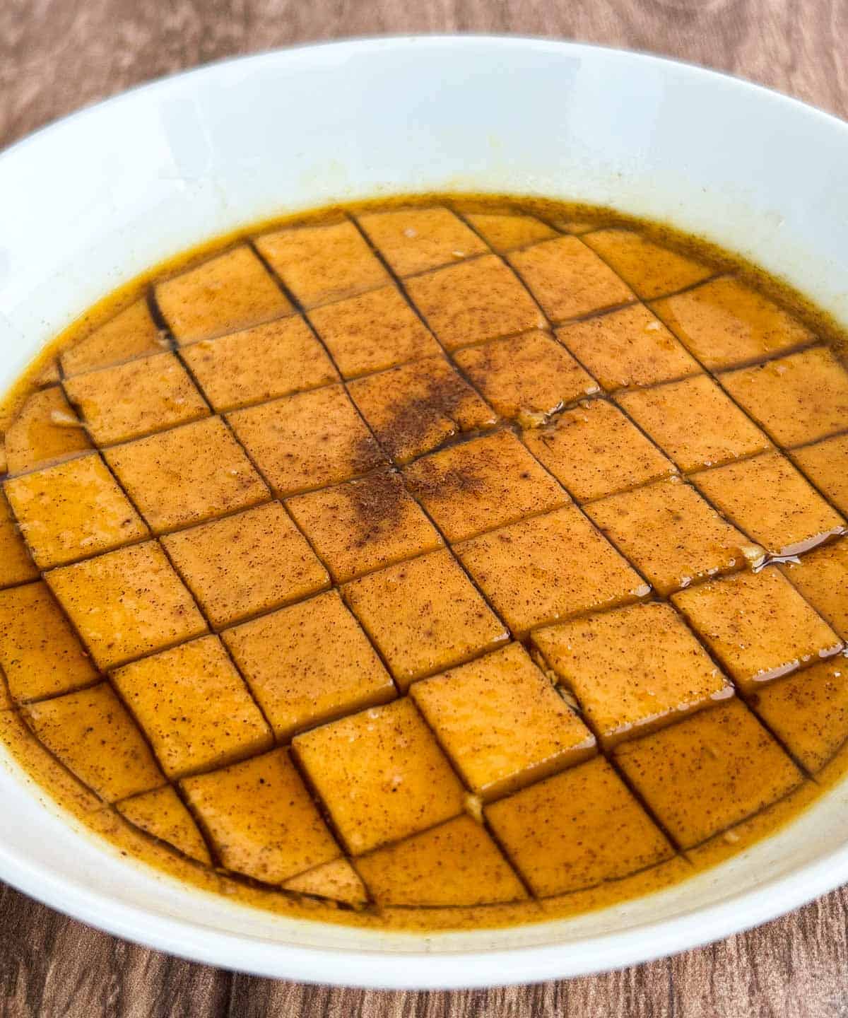 pumpkin flan cut into squares topped with brown sugar syrup and pumpkin spice.