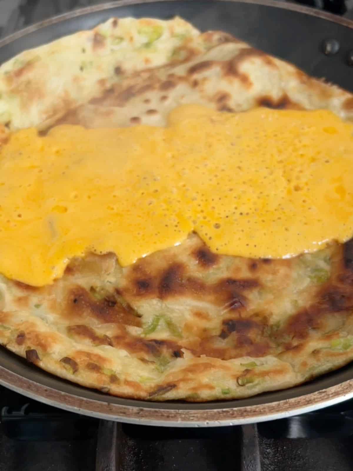 Scallion pancake in a skillet with melted cheddar cheese on top.