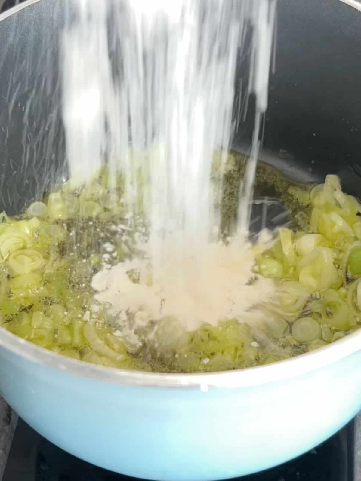 Cooking scallion whites in oil and adding flour to the mixture.