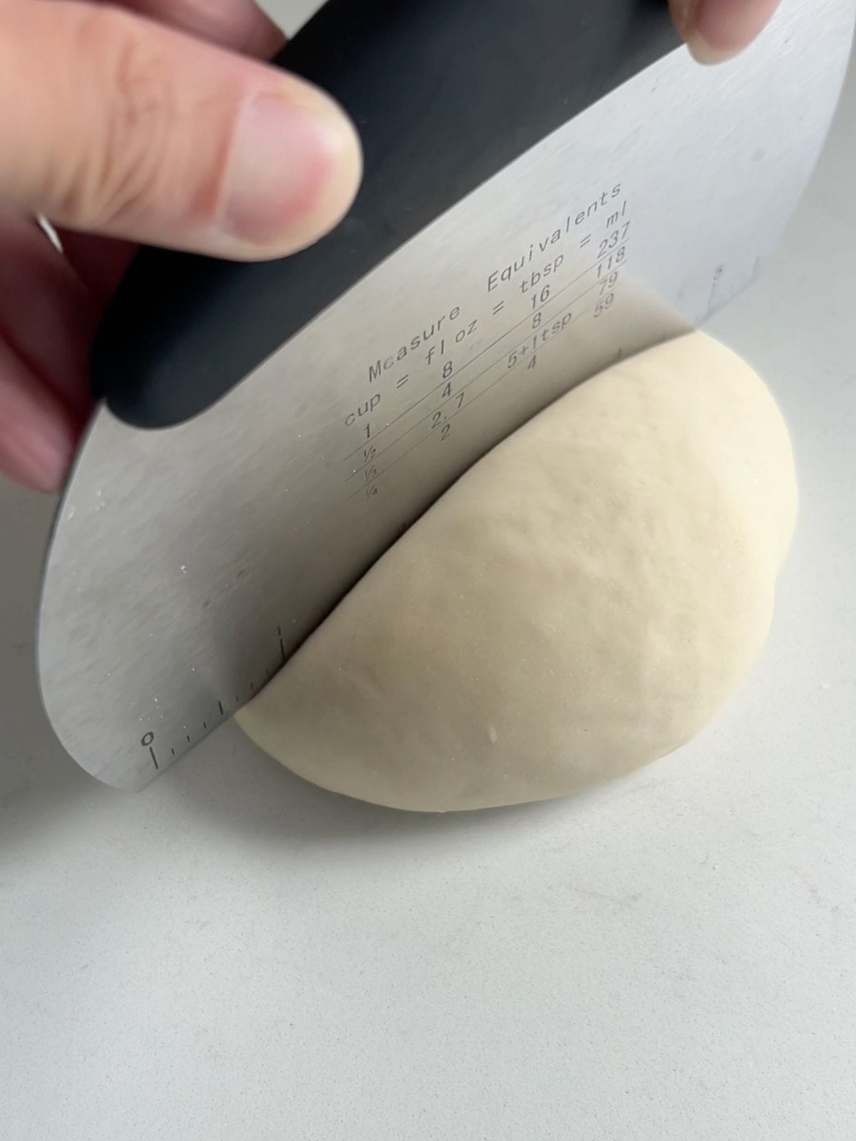 Slicing a ball of dough into two pieces using a bench scraper.