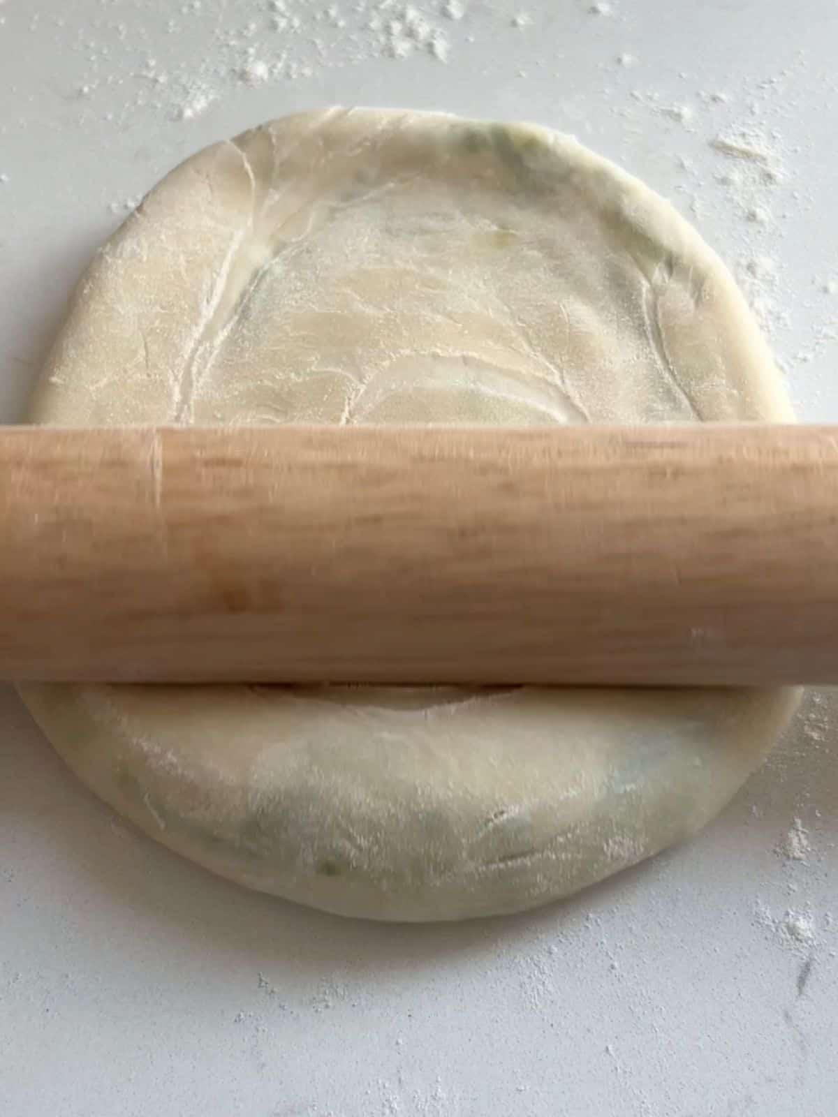 Using a rolling pin to roll out the scallion pancake dough into a pancake.