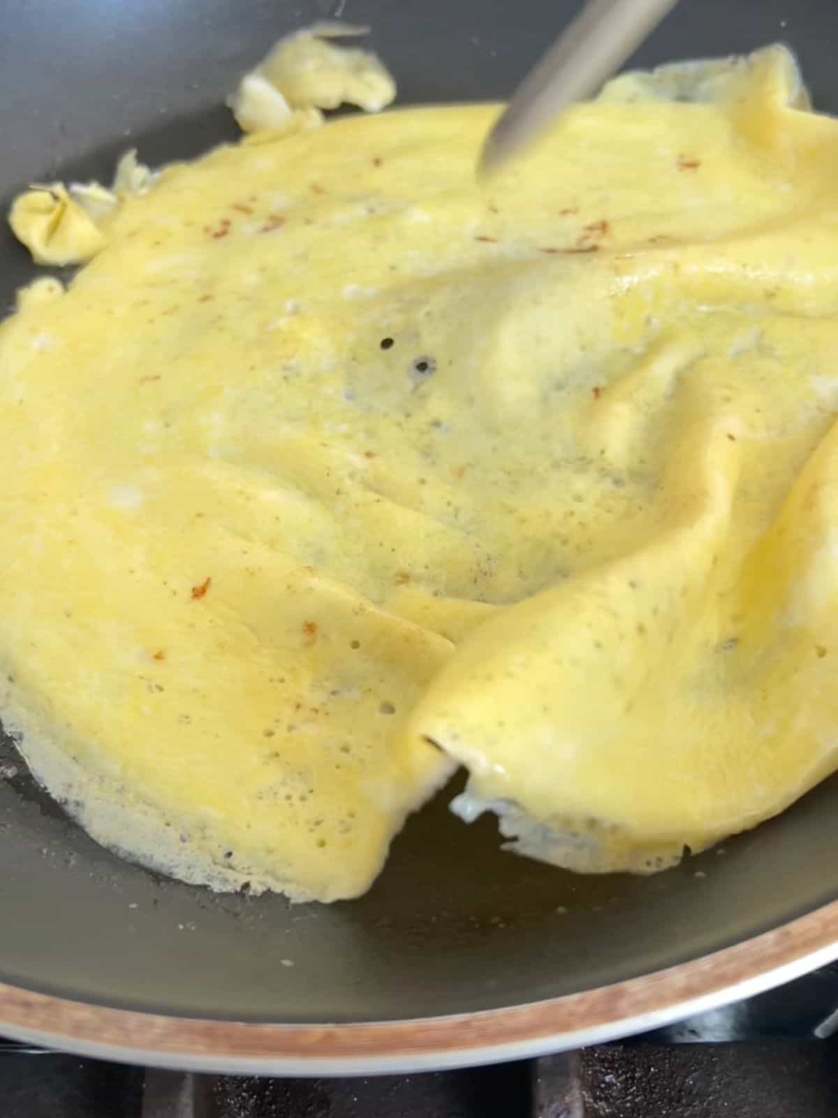 Thin layer of eggs being flipped in a skillet.