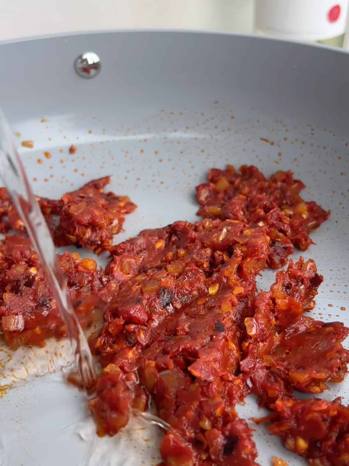 Vodka being added to the tomato mixture in a skillet.