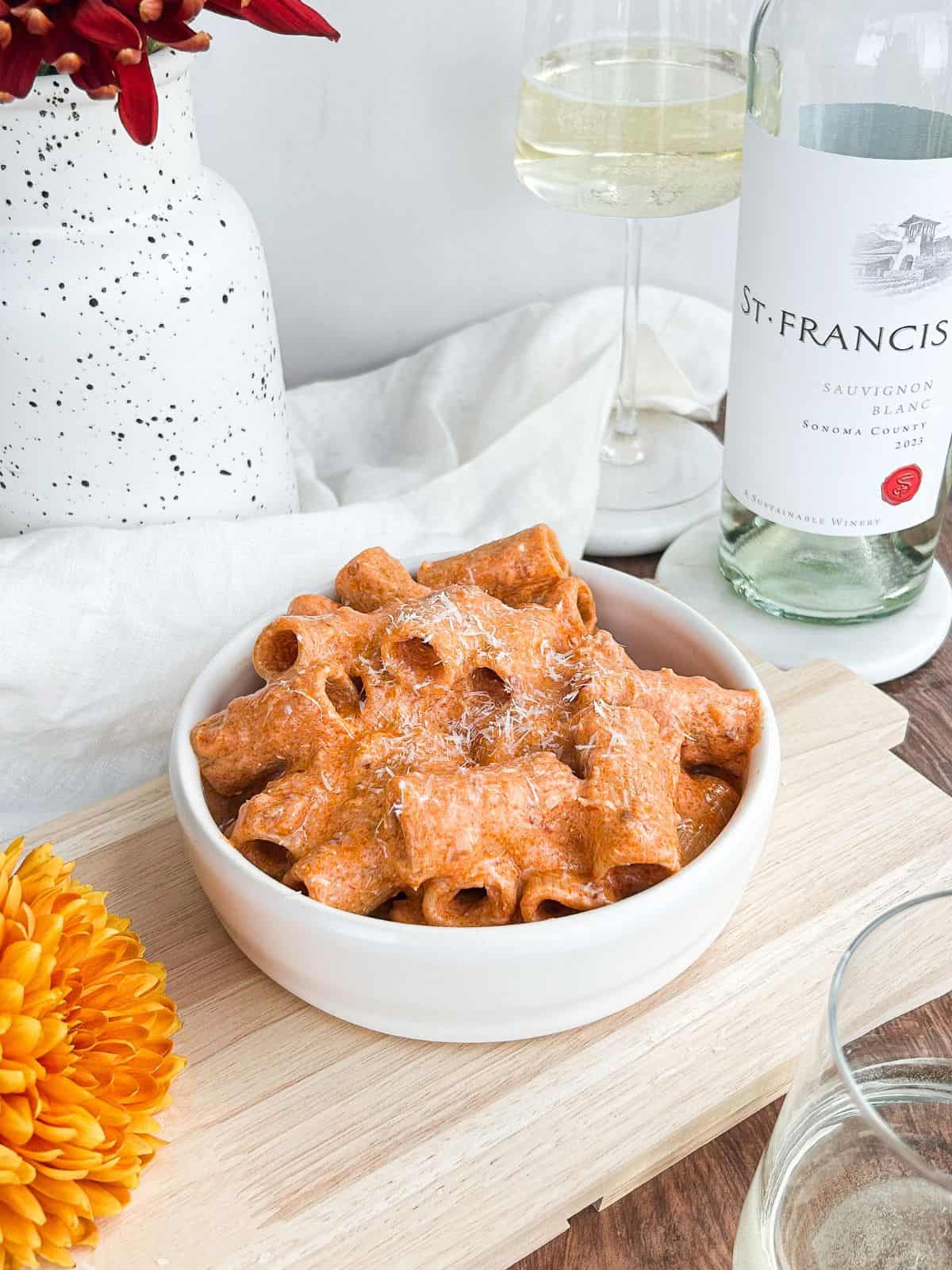 Spicy vodka pasta served in a white bowl on a wooden cutting board with a glass of wine behind it.