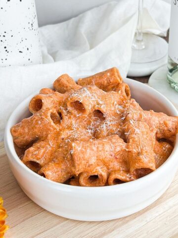 Bowl of high protein spicy vodka pasta with a bottle of white wine in the background.