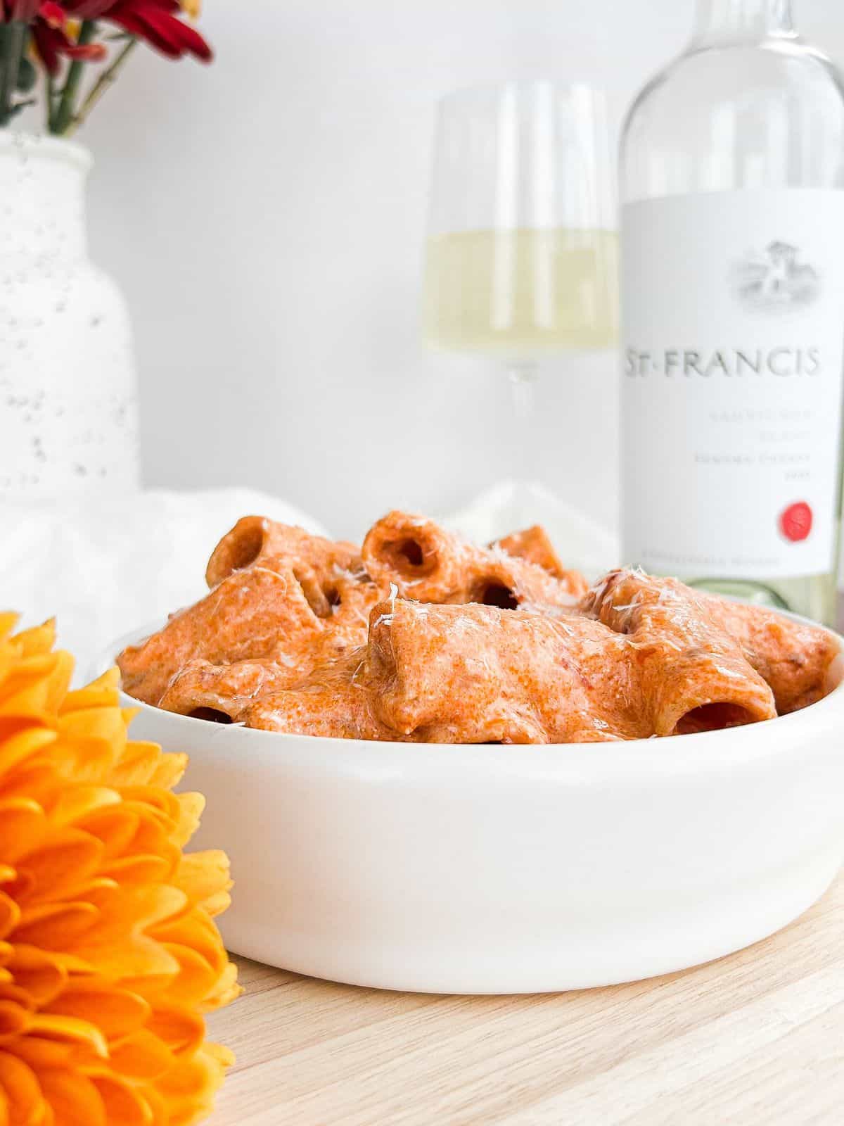 Side view of high protein spicy vodka pasta in a white bowl on a wooden background.