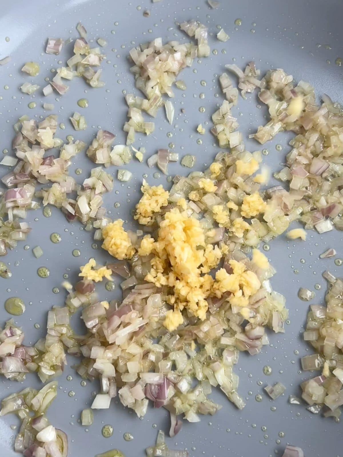 Shallots and garlic being sautéed in a skillet with olive oil.