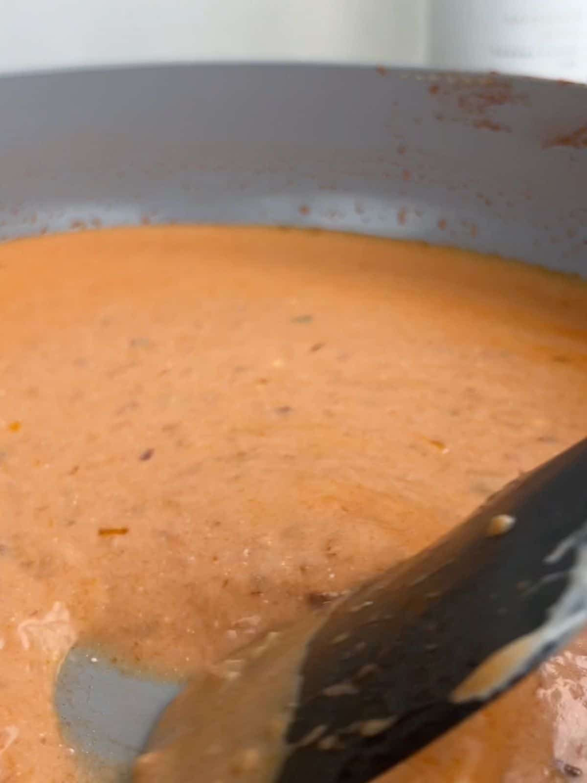 Creamy tomato vodka sauce in a pan being stirred with a rubber spatula.