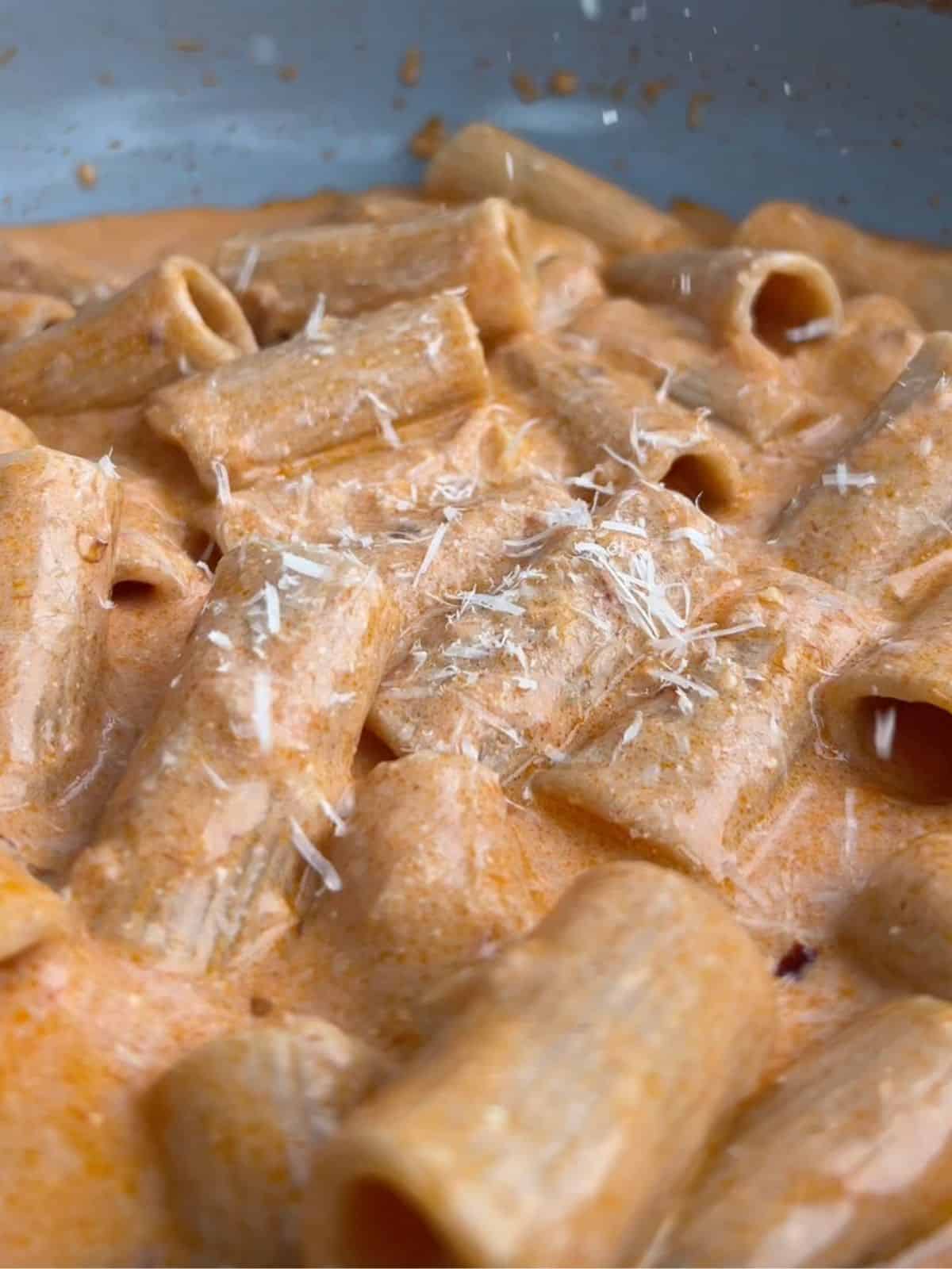 Spicy vodka pasta in a pan with parmesan being sprinkled on top.