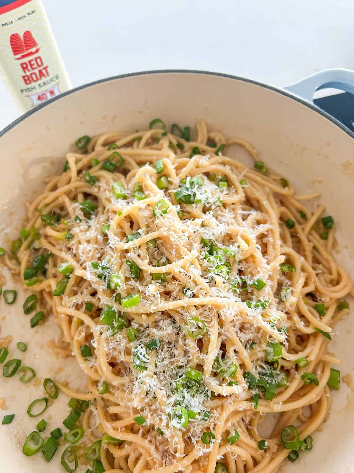 Vietnamese garlic noodles in a pan topped with scallions and parmesan cheese. 