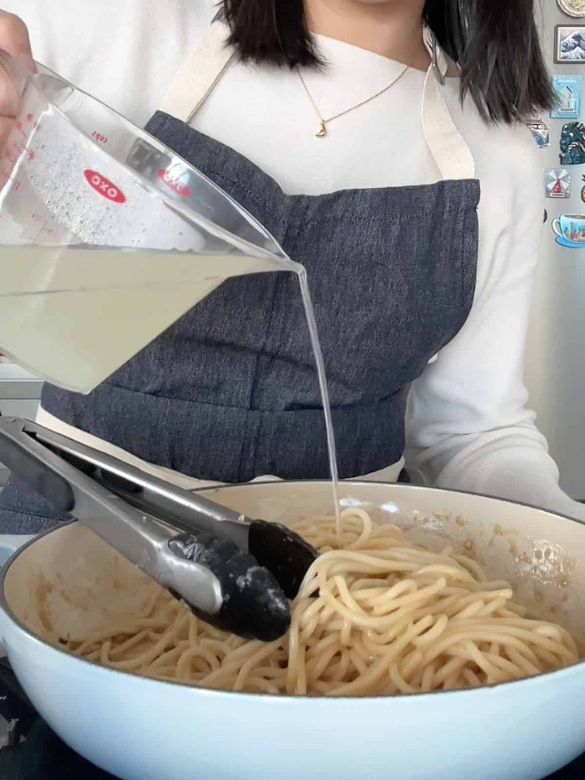 Pouring the reserved pasta water into the noodles in the skillet. 