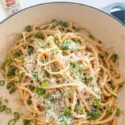 Pile of Vietnamese garlic noodles in a pan topped with scallions and freshly shredded parmesan cheese.