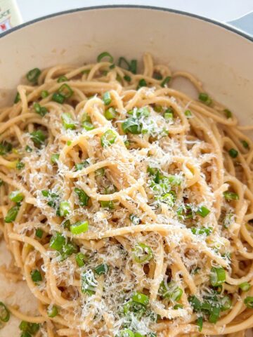 Pile of Vietnamese garlic noodles in a pan topped with scallions and freshly shredded parmesan cheese.