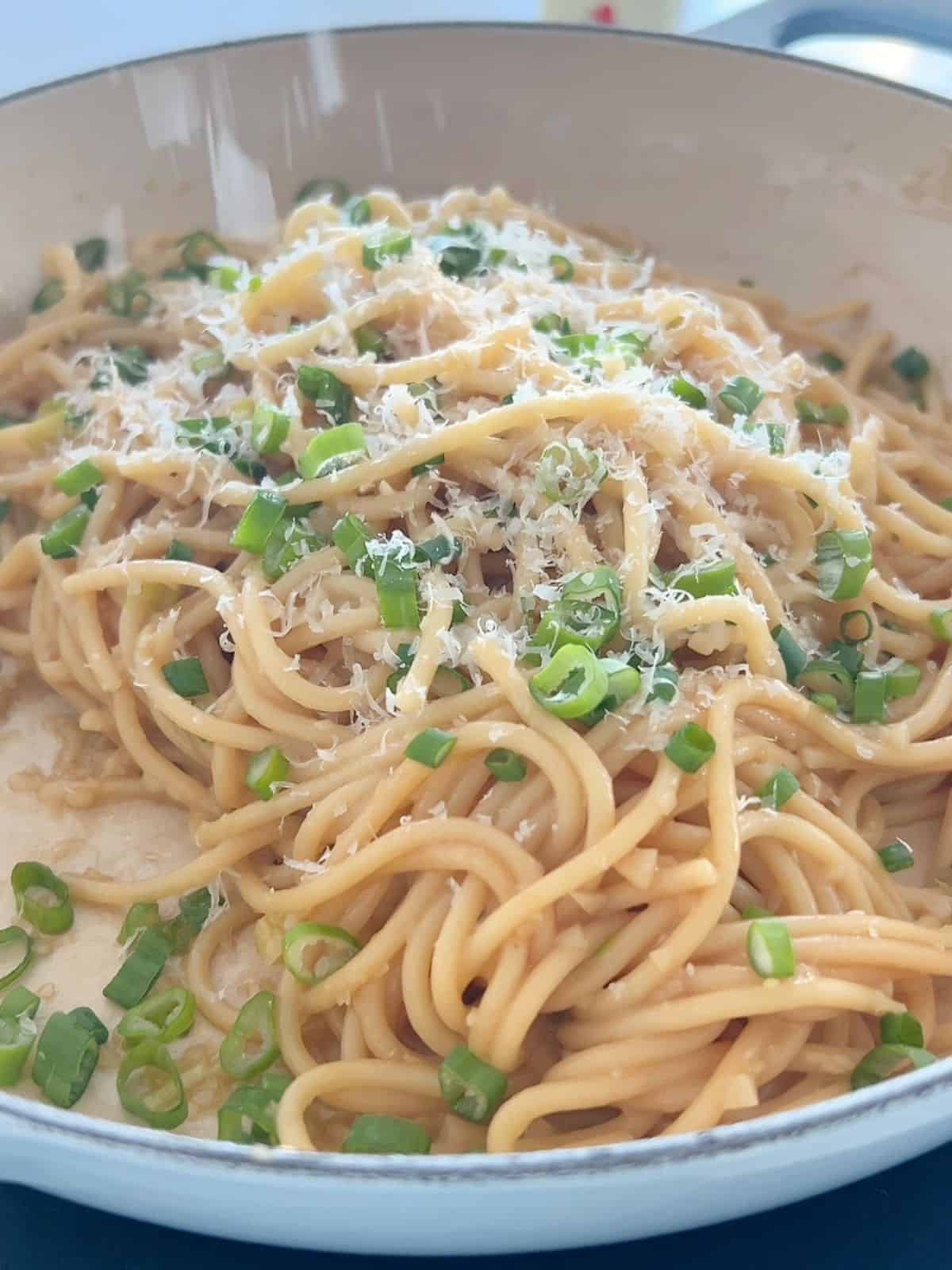 Vietnamese garlic noodles in the skillet after being cooked and topped with scallions and parmesan. 