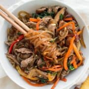 Overhead shot of beef japchae with noodles twirled around chopsticks.