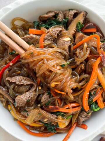 Overhead shot of beef japchae with noodles twirled around chopsticks.