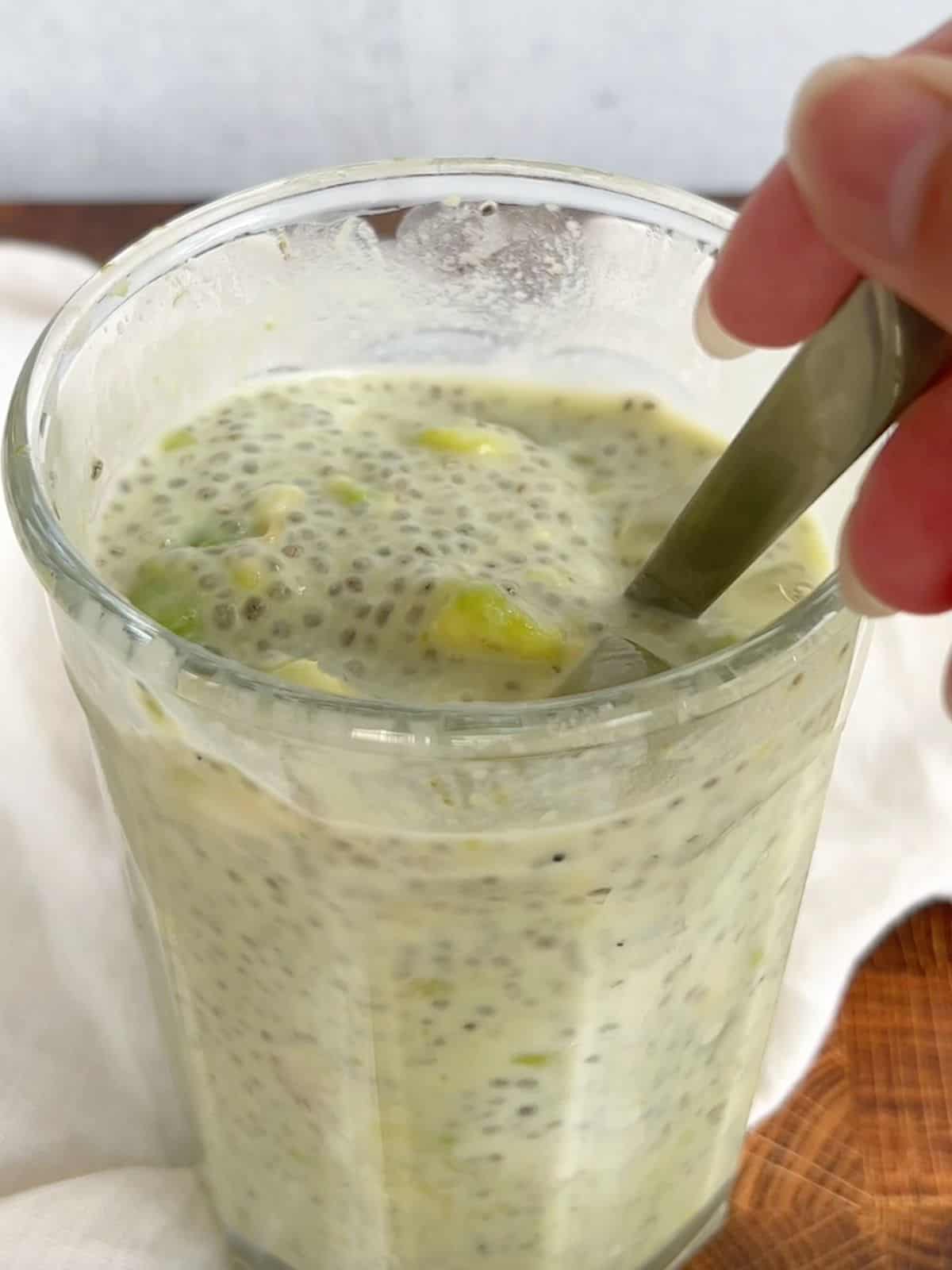 Stirring the avocado chia pudding in a glass with a spoon.