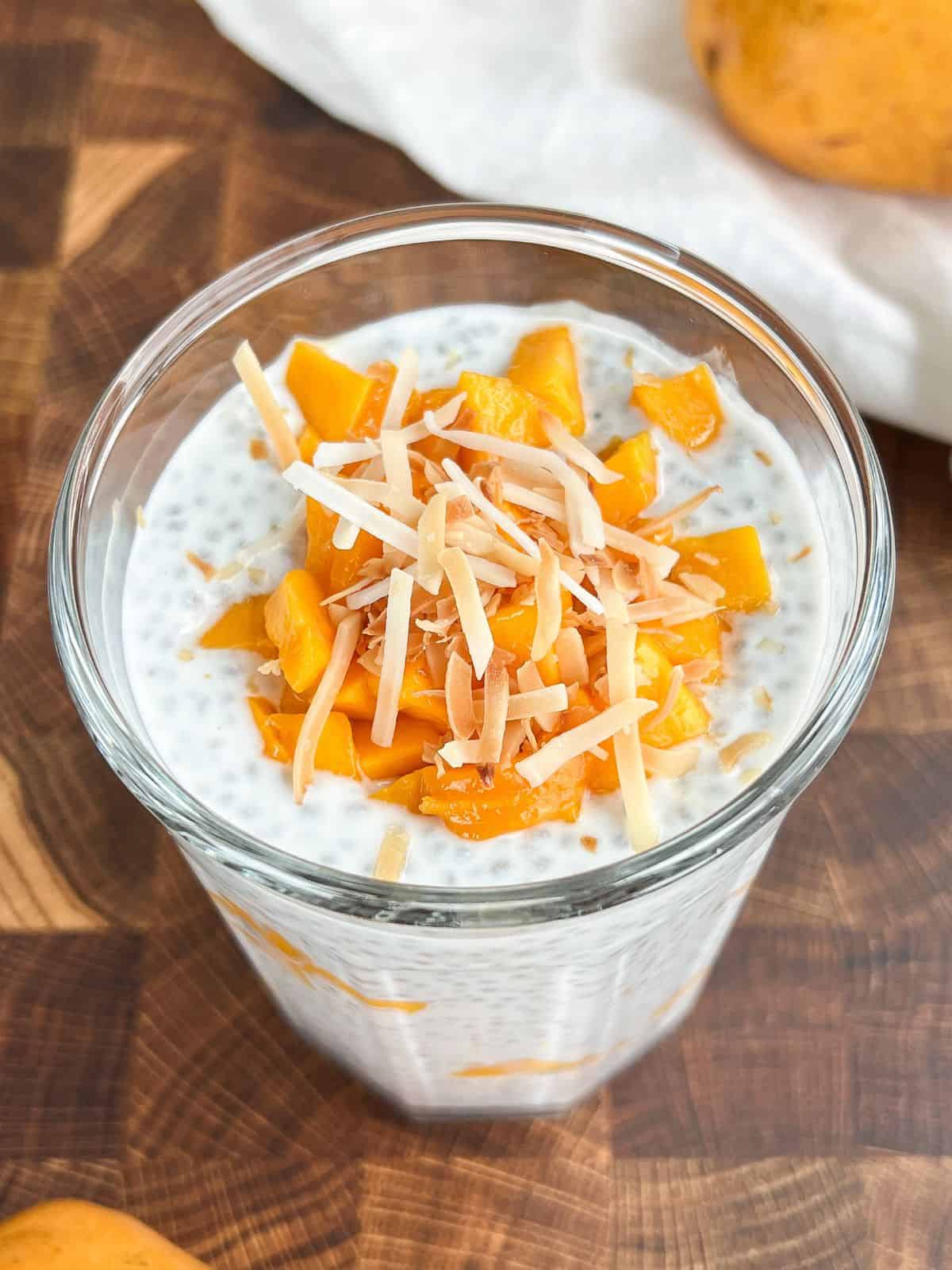 Mango chia pudding in a glass with fresh mango and coconut flakes on top.