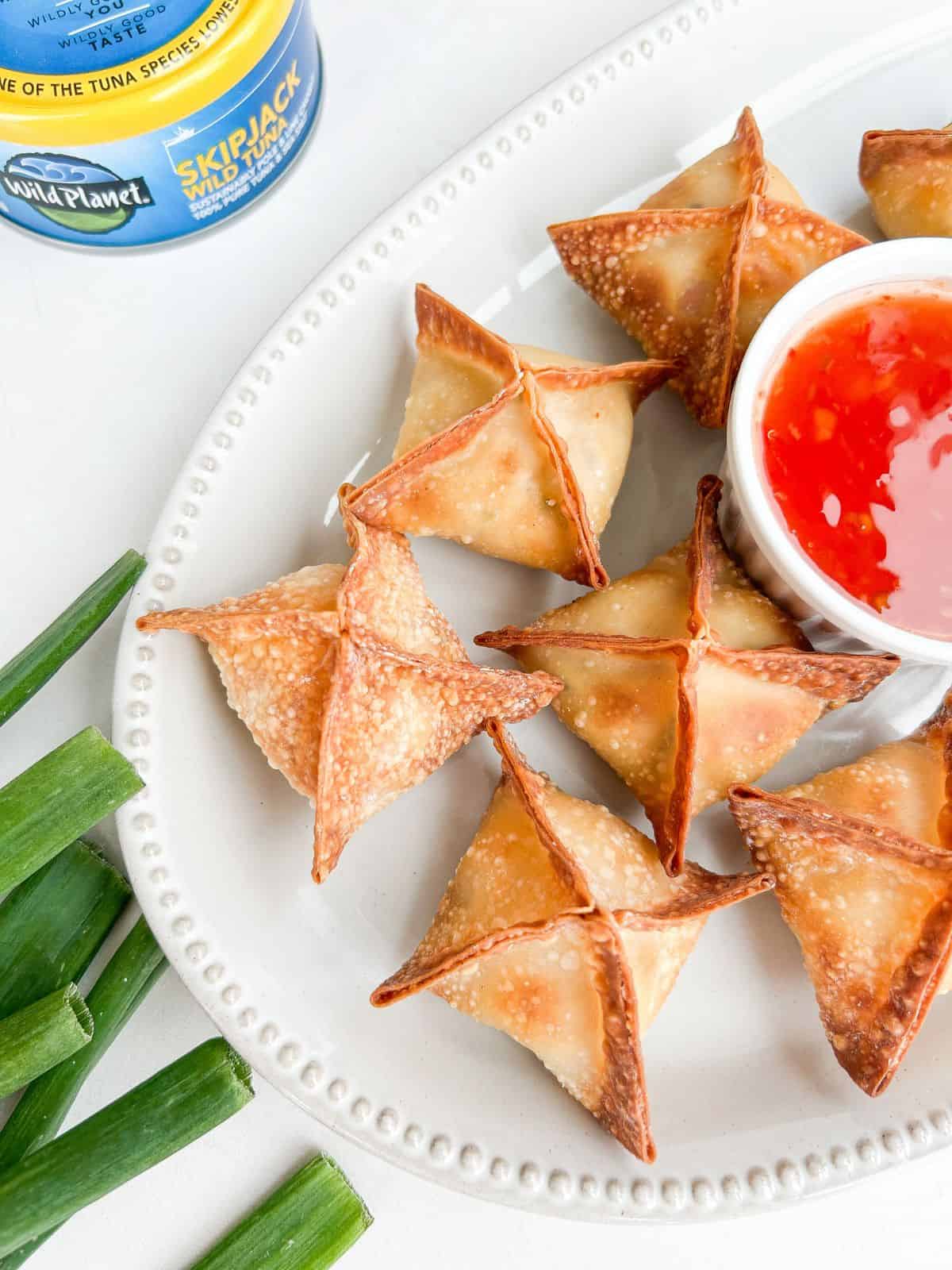 Overhead shot of tuna cream cheese wontons on a serving plate with a side of dipping sauce.