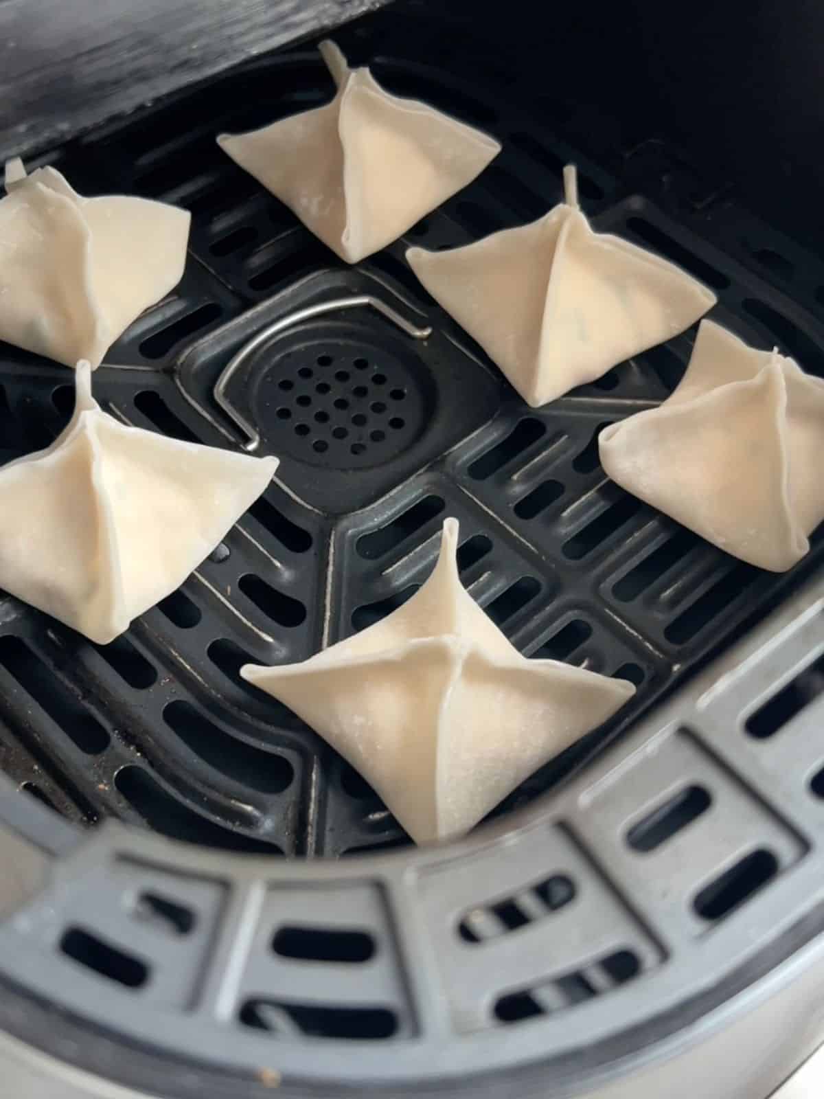 Wontons in an air fryer basket before being cooked.