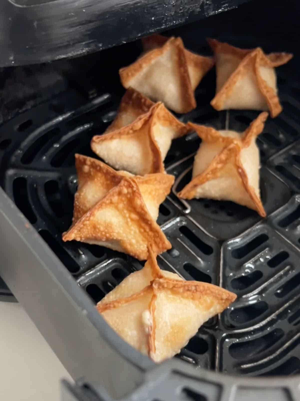 Tuna cream cheese wontons in an air fryer basket after being cooked.