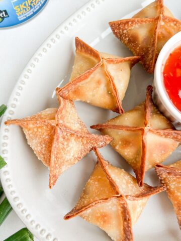 Overhead shot of cream cheese tuna wontons on a place served with a red sauce.