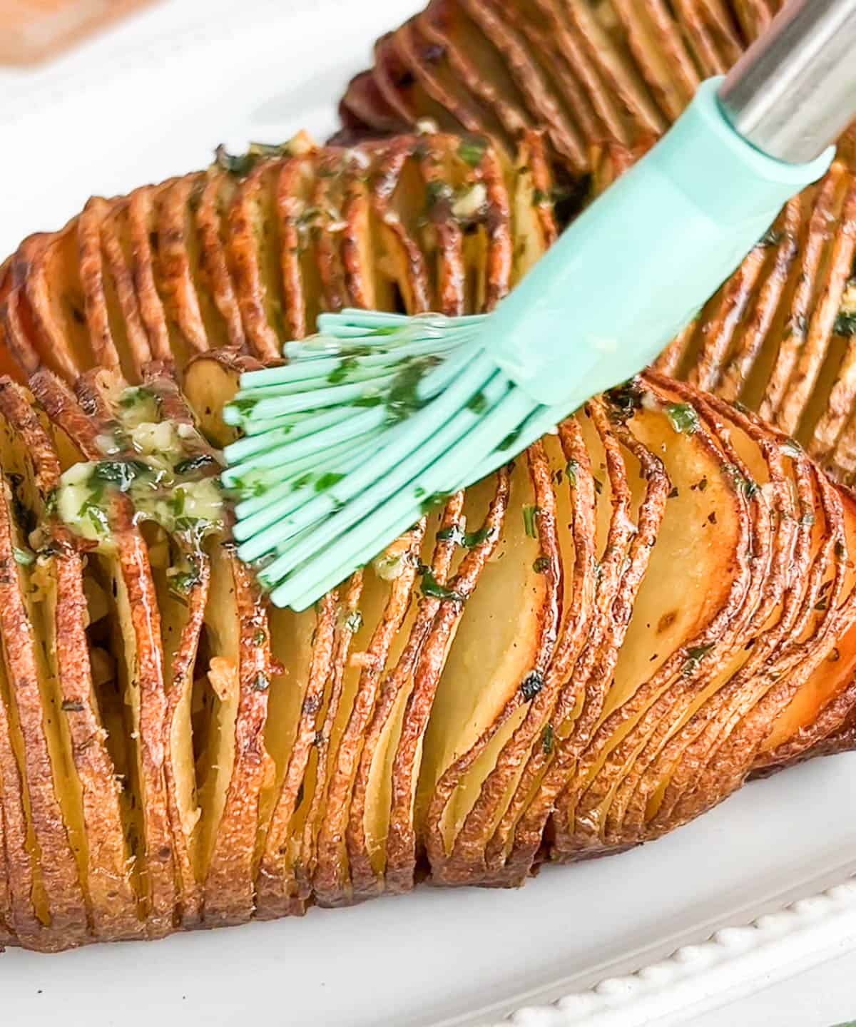 Shot of fish sauce butter being brushed onto hasselback potatoes.