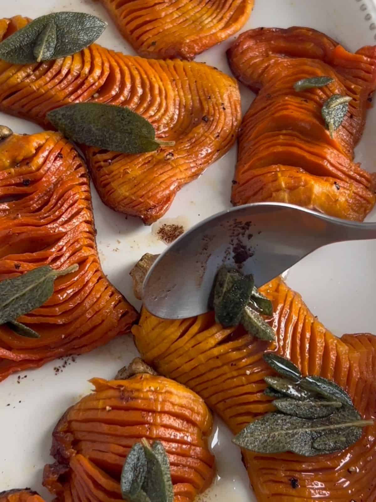 Using a spoon to place the brown butter and sage mixture on top of the baked squash.