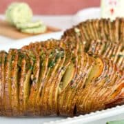 Side view of hasselback potatoes served on a white plate with butter in the background.