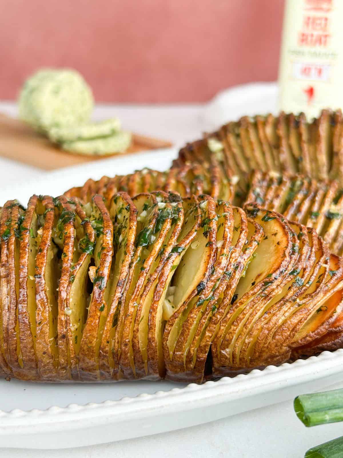 Hasselback potatoes served on a white serving platter with butter and fish sauce in the background.