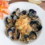 Overhead shot of clams and spaghetti topped with breadcrumbs with a flower in the corner.