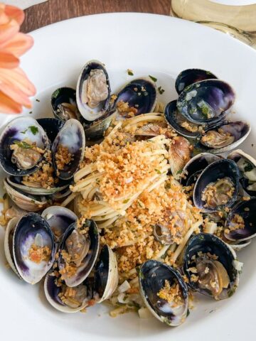 Overhead shot of clams and spaghetti topped with breadcrumbs with a flower in the corner.