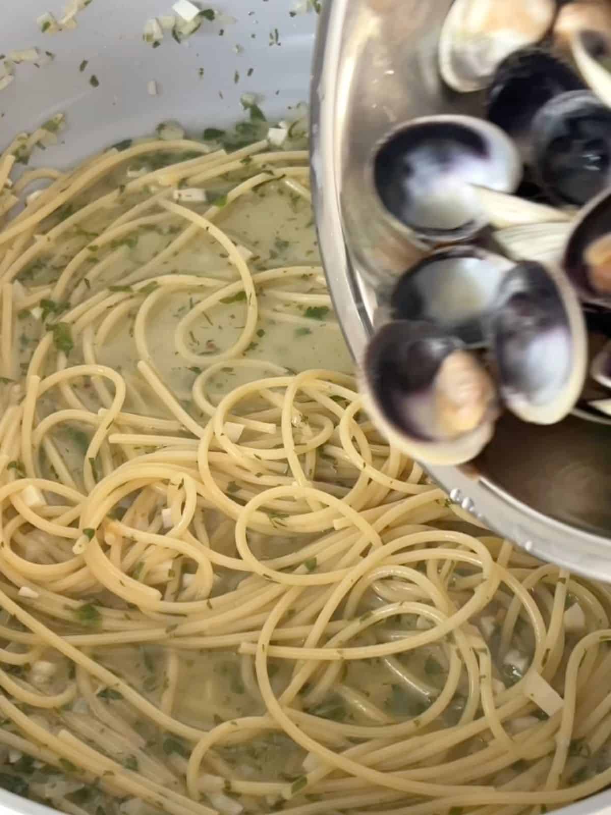 Cooked clams being added back into the skillet with spaghetti and wine sauce.