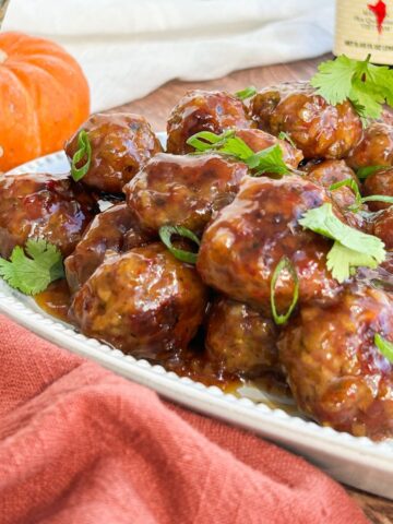 Sweet chili cocktail meatballs on a serving platter garnished with scallions and cilantro.