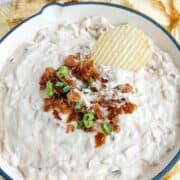 French onion dip in a white bowl topped with caramelized onions, scallions, and a ruffle potato chip.