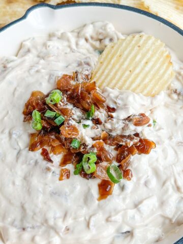 French onion dip in a white bowl topped with caramelized onions, scallions, and a ruffle potato chip.